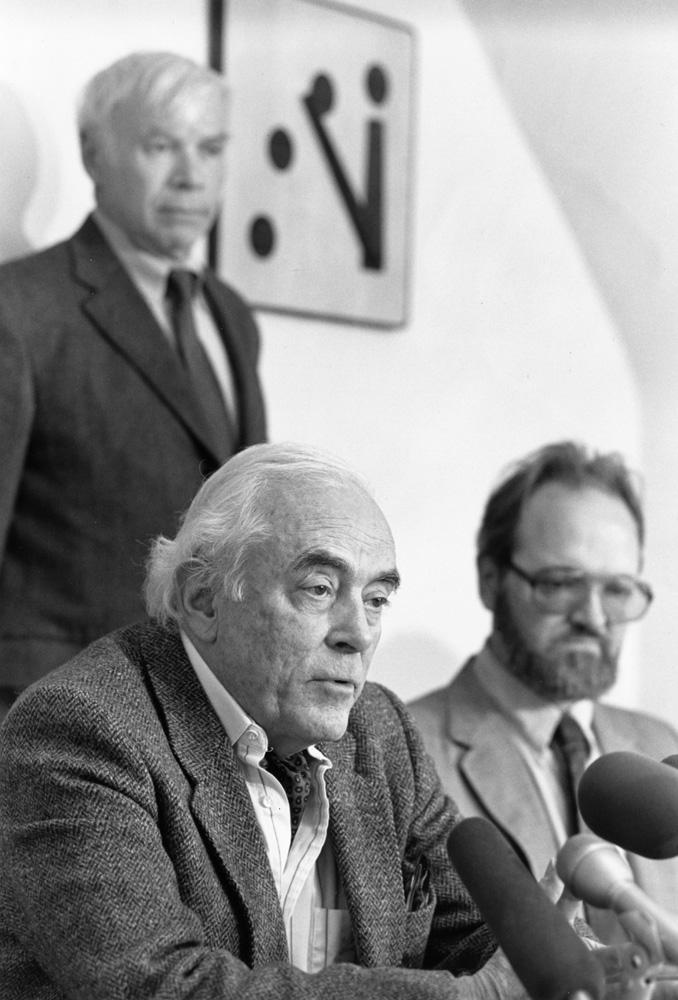 Three men in suits with the iconic Doomsday Clock behind them