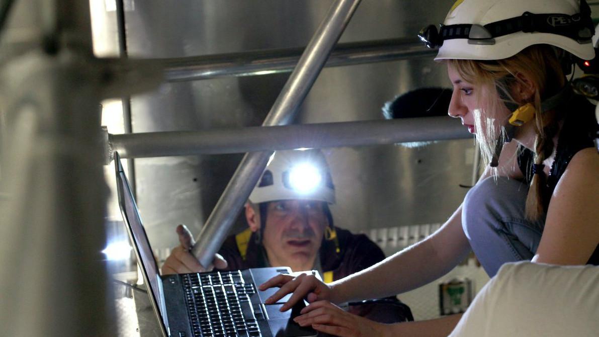 Two scientists with safety hats and headlamps, one at a computer